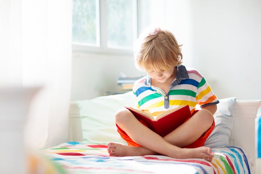 Child reading book in bed. Kids read in bedroom.