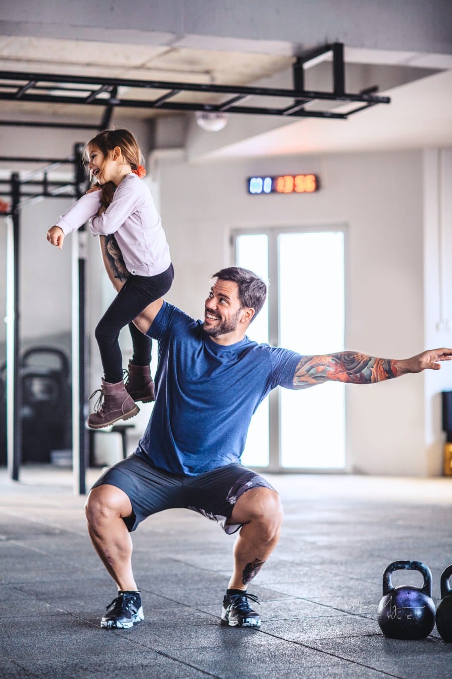 father doing training in the gym while using his young daughter as a weight on his arm