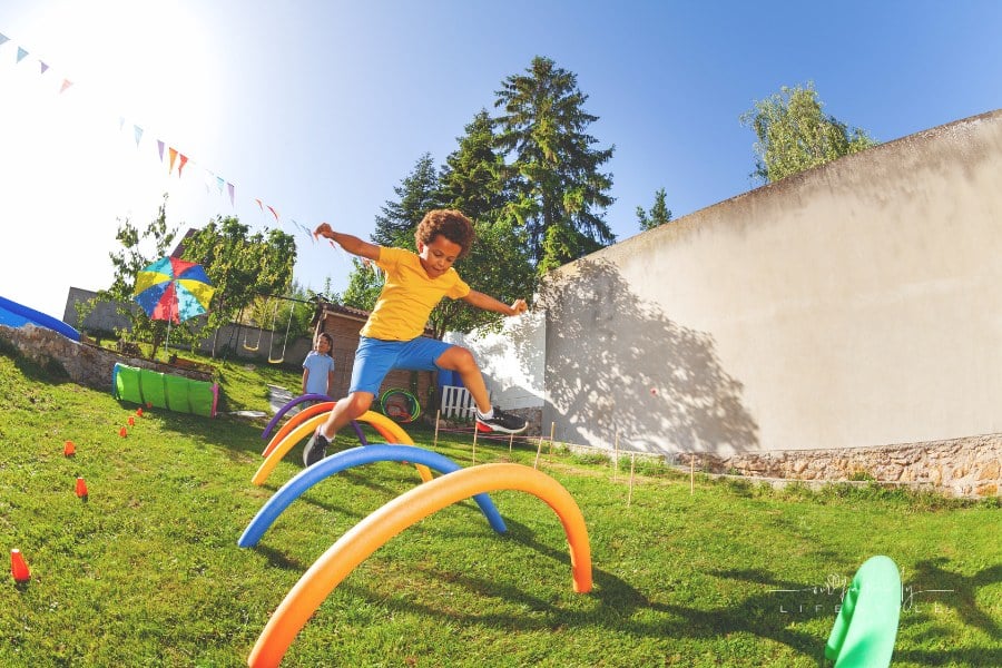 Portrait of a cute curly boy jump over obstacle course barriers playing competition game
