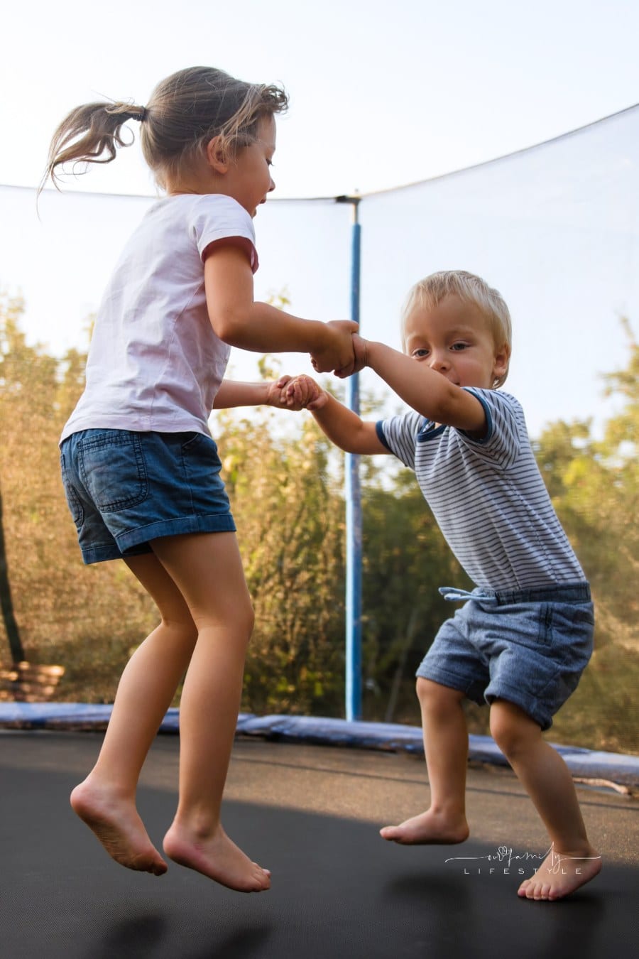 Adorable siblings holding hands and bouncing together on trampoline