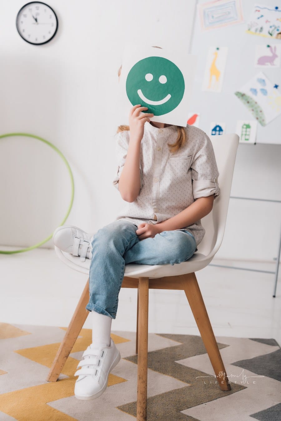 child sitting on chair and covering face with smiling face symbol