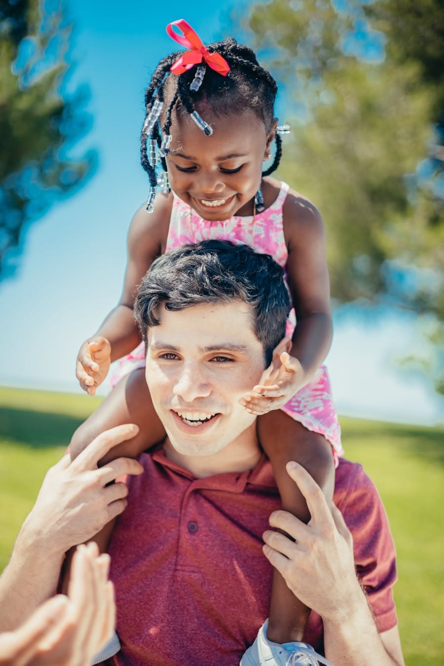 Father with daughter on shoulders enjoying a sunny day outdoors, showcasing love and happiness.