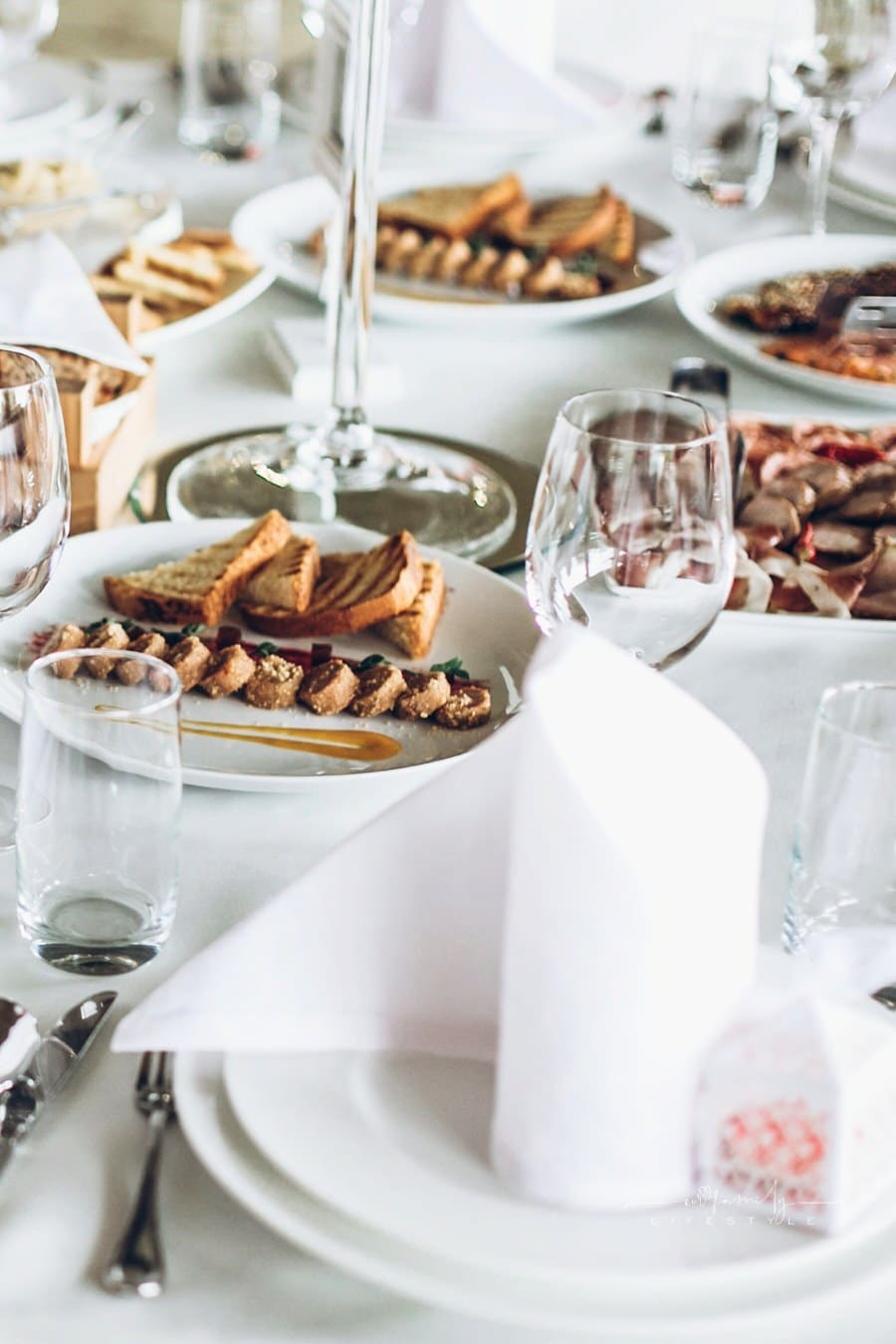 luxury catering for wedding reception. elegant wedding table with food, silver cutlery, empty glasses, white silk chairs and napkins. stylish wedding table setting