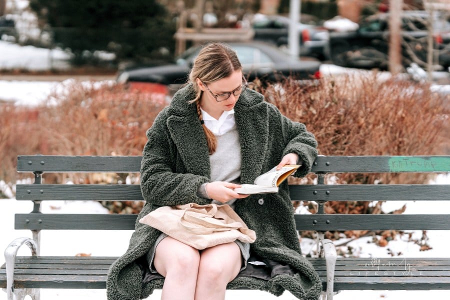 Serious woman reading book on park bench on snowy street