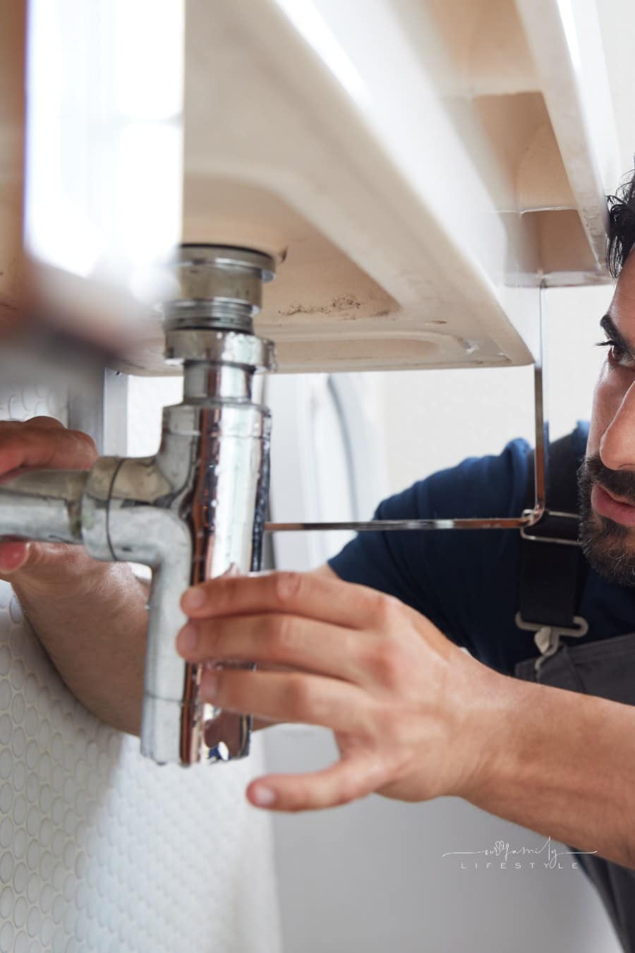 Male Plumber Working to Fix Leaking Sink in Home Bathroom
