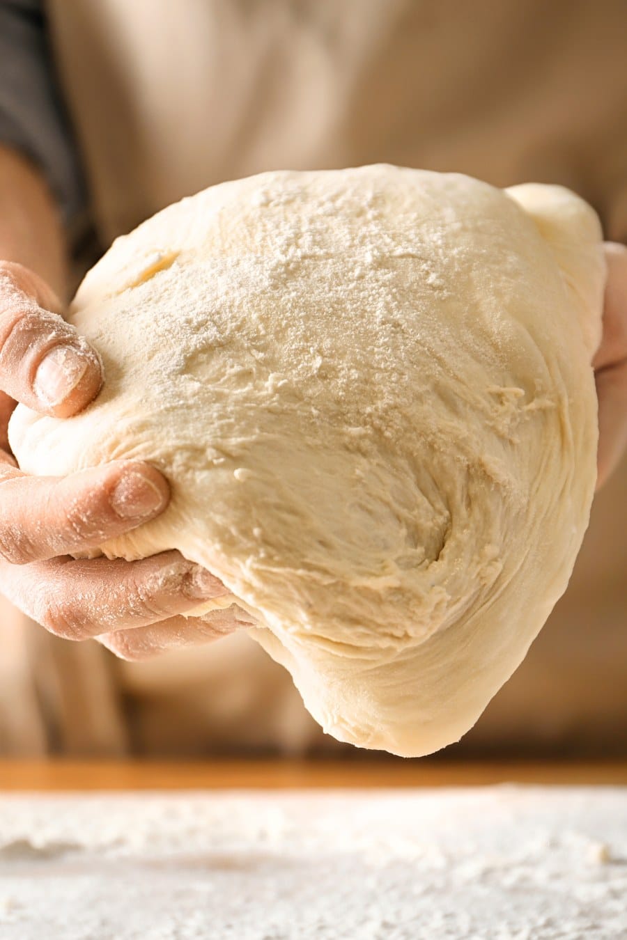 Woman holding dough above table sprinkled with flour