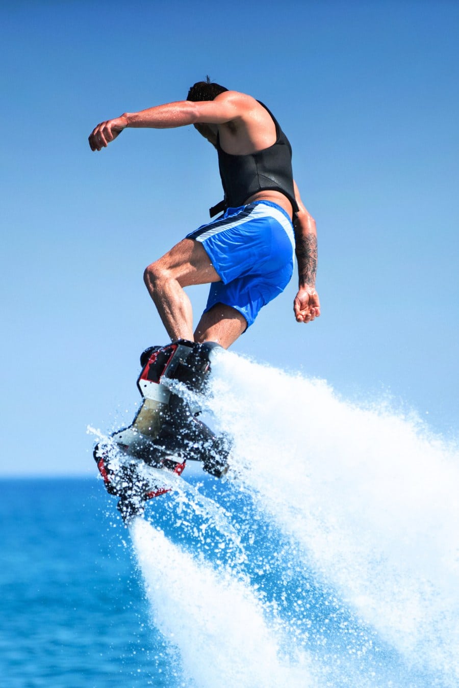 Closeup side view of a young man enjoying flyboarding session at sea on a sunny summer day.