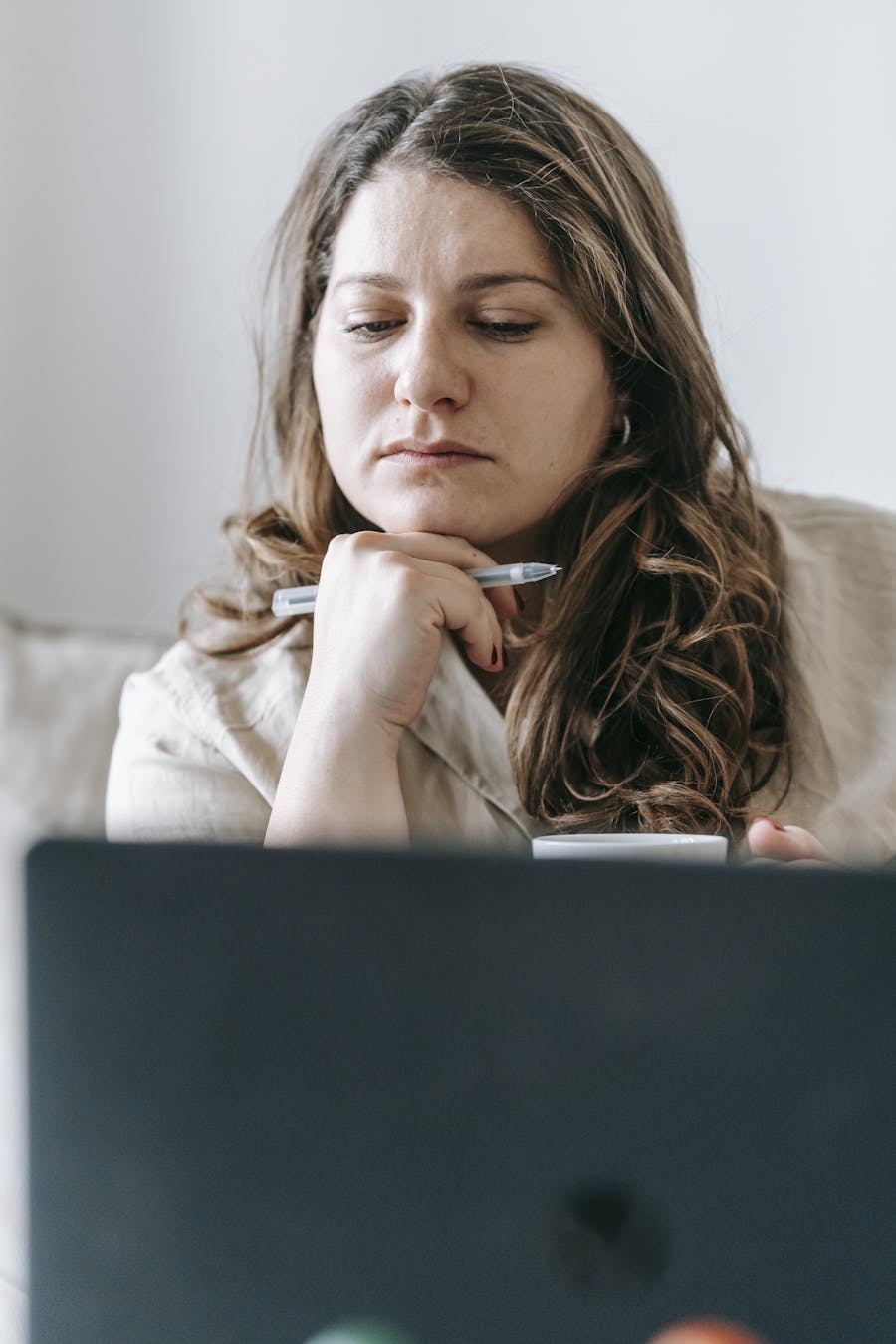 Focused woman in casual setting working on laptop from home, deep in thought.