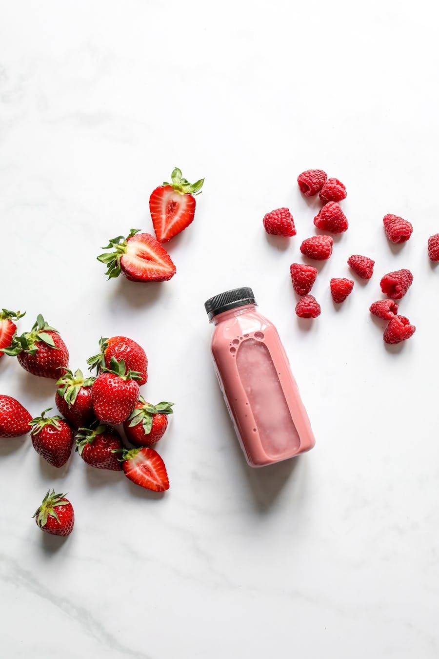 Fresh strawberry and raspberry smoothie in a plastic bottle on a white background, ideal for food photography.
