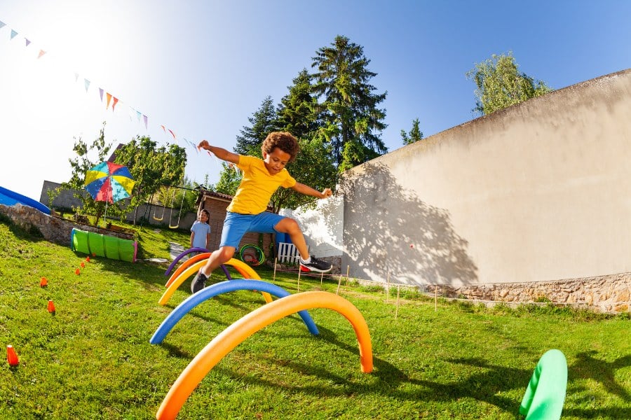 boy jumping over pool noodles being used as outdoor obstacle course