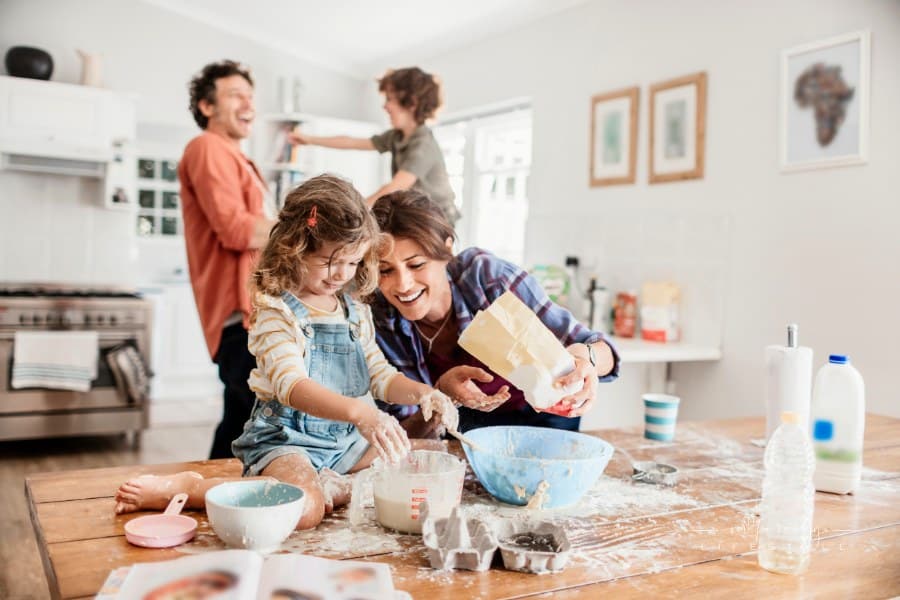 Young family baking together in kitchen covered in baking ingredients