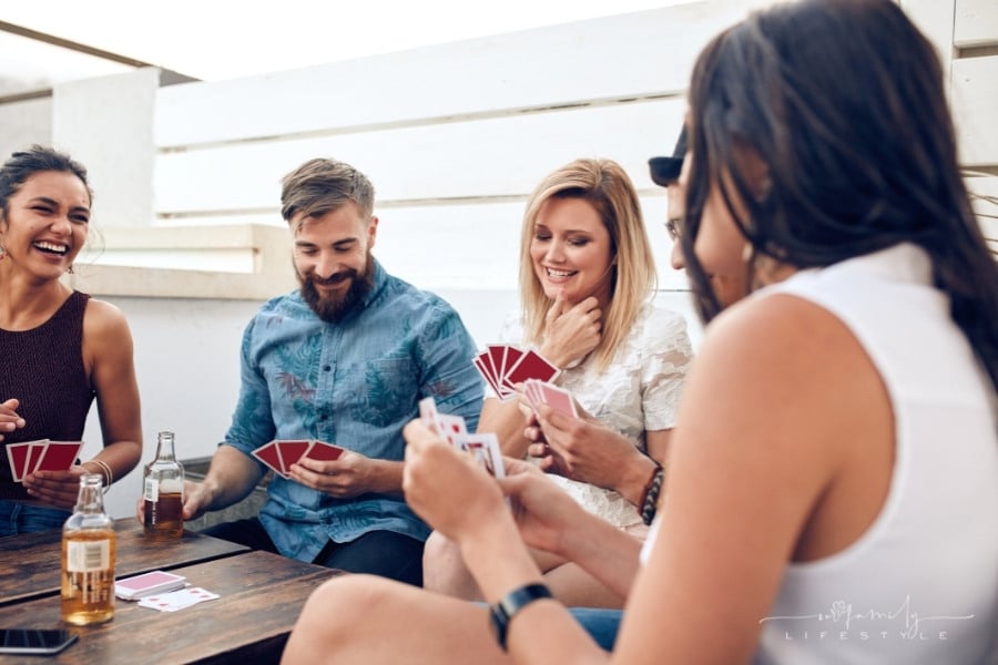 group of friends sitting at wooden table playing card game