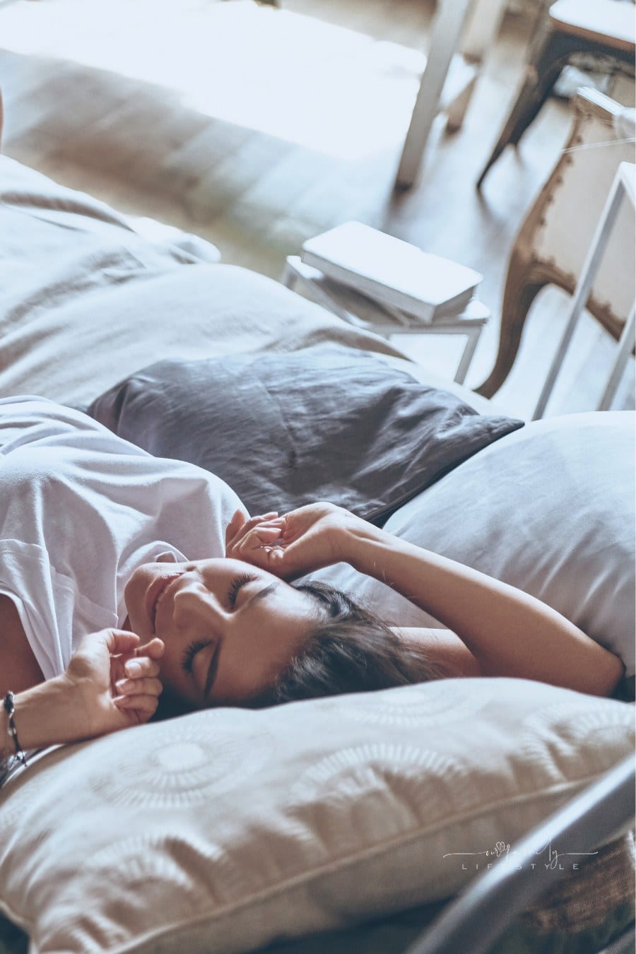 young woman keeping eyes closed and smiling while stretching in the bed at home