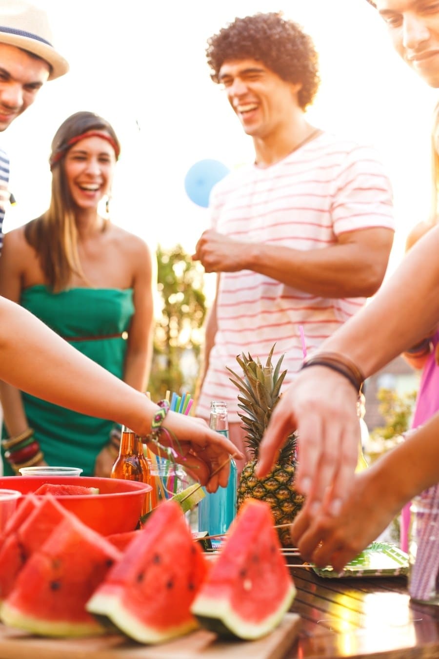 group of young people enjoying a rooftop summer party with watermelon slices and pineapple