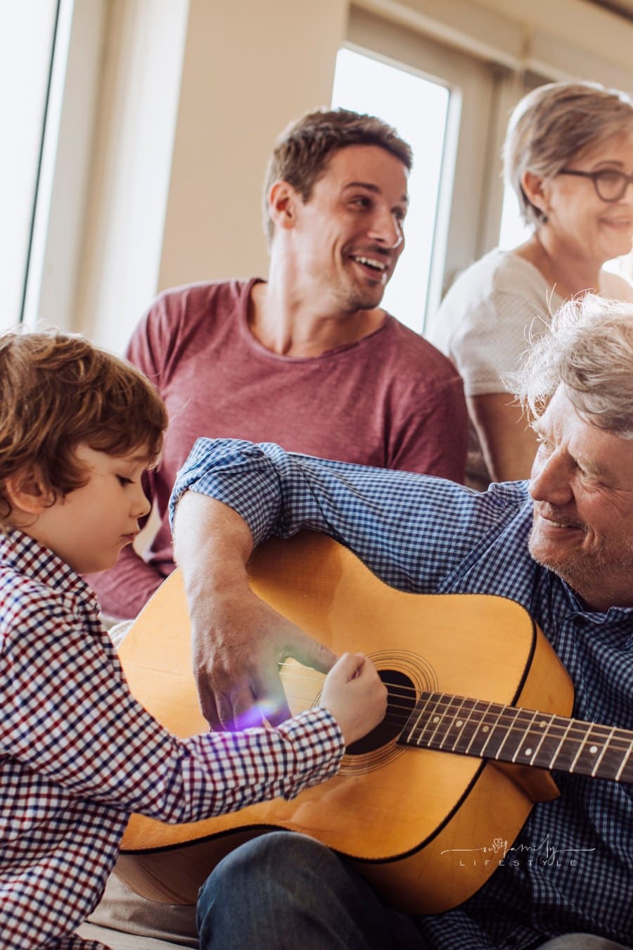 Multi-generation family gathering with grandfather playing guitar while grandchildren look on