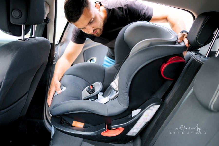 man installing child car seat into back seat of car