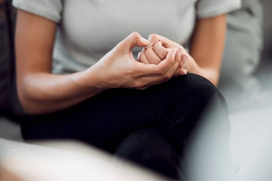 Cropped shot of an unrecognisable woman sitting alone and feeling anxious while picking the skin on her nails.
