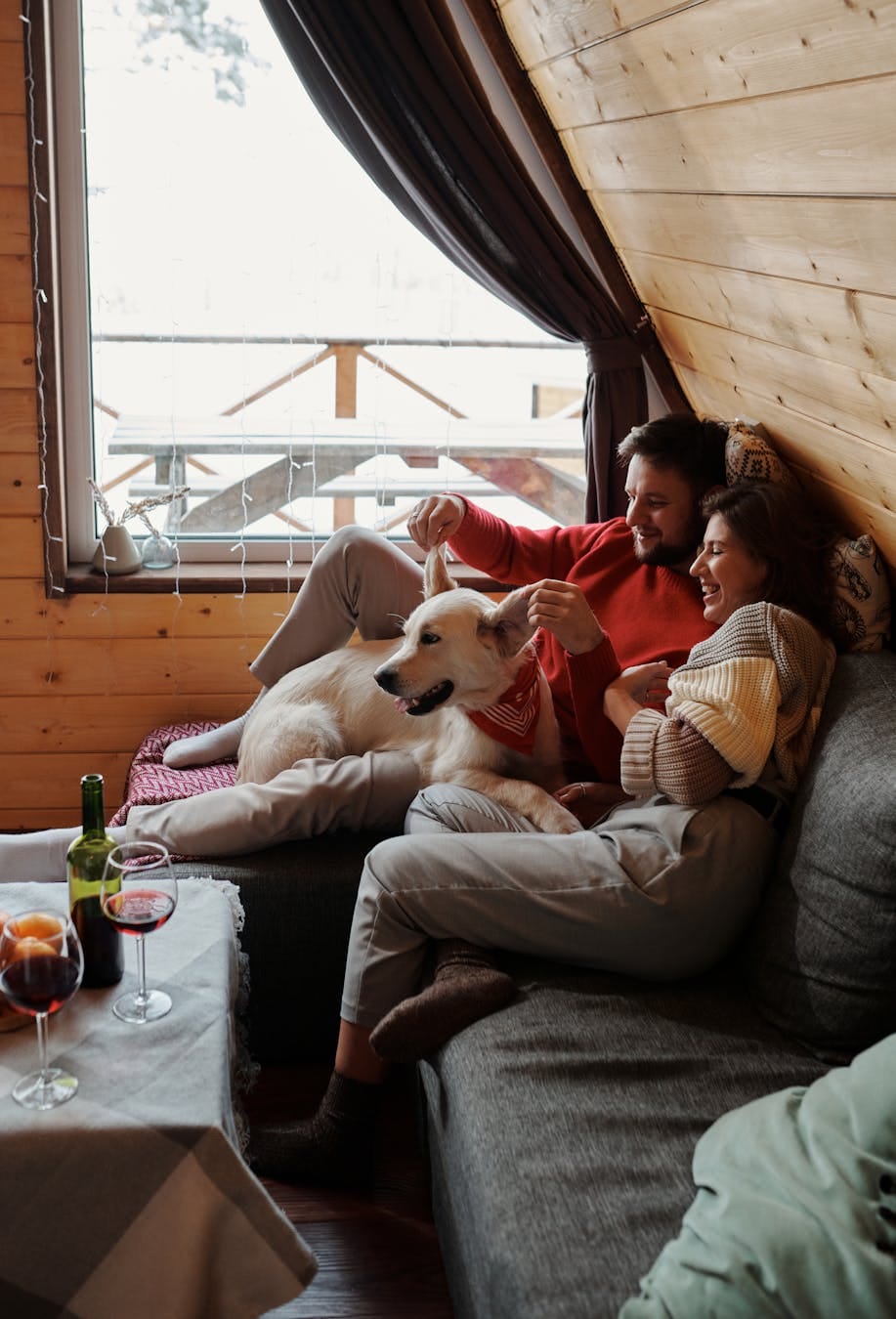 Happy couple enjoying leisure time with their dog in a cozy wooden cabin with wine. Warm and inviting atmosphere.
