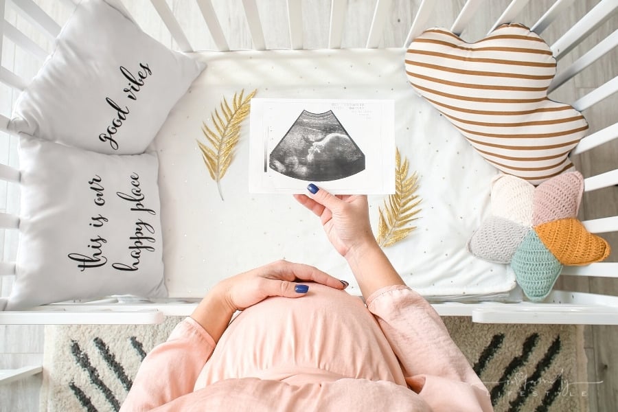 pregnant woman with one hand on stomach and other holding a sonogram over a crib