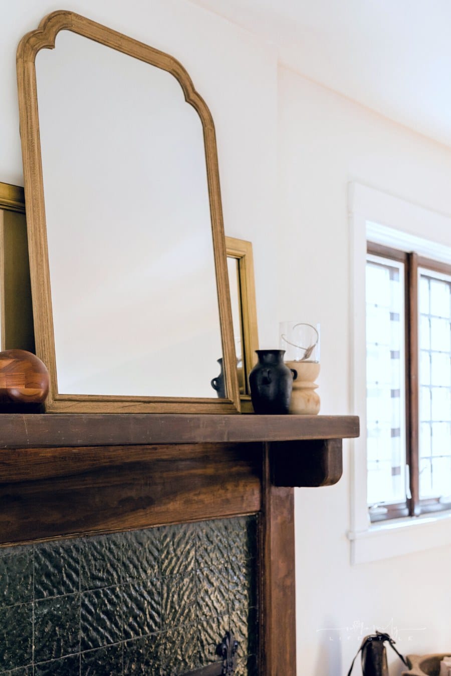 vintage mirror on a fireplace mantel surrounded by traditional wood home décor accents