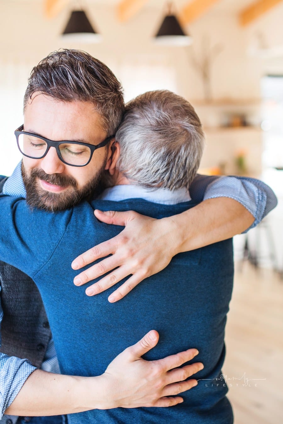 An Adult Son and Senior Father Indoors at Home, Hugging.