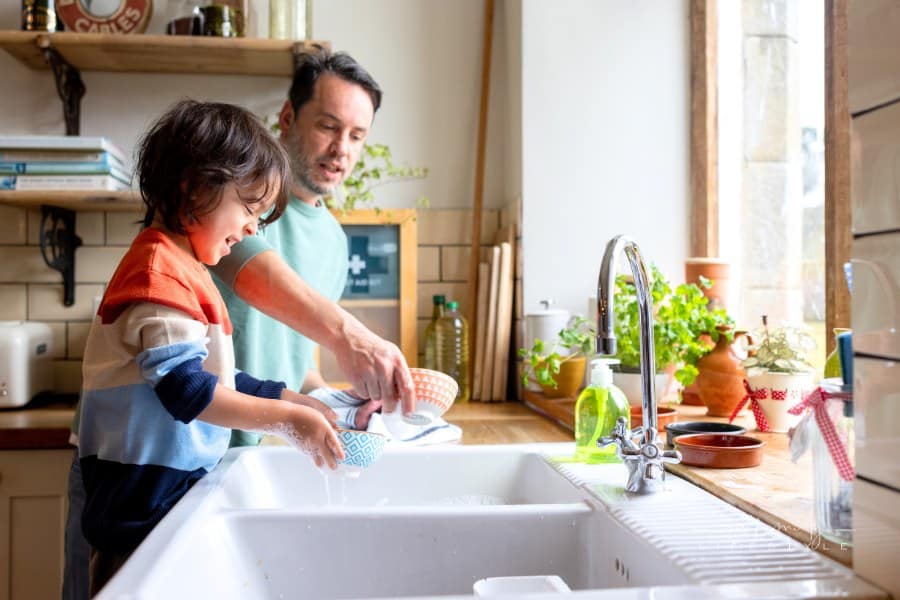 Father and son washing dishes in kitchen sink