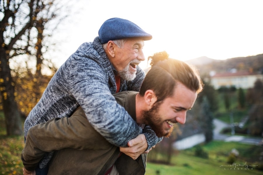 adult son carrying senior father outdoors with both laughing