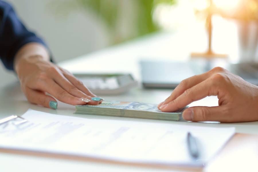 hands passing cash over a contract on the desk