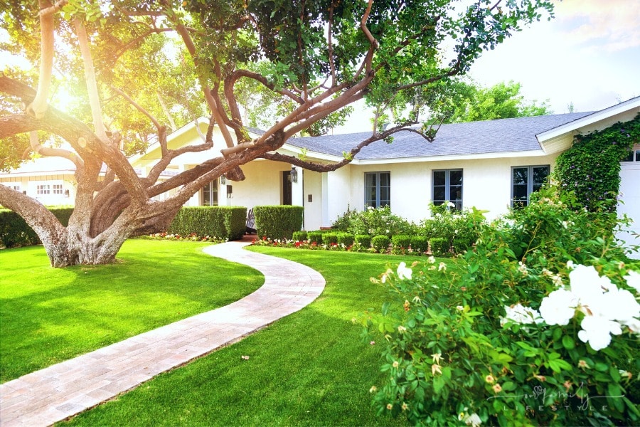 residential home with big yard covered in green grass, large trees and flowers
