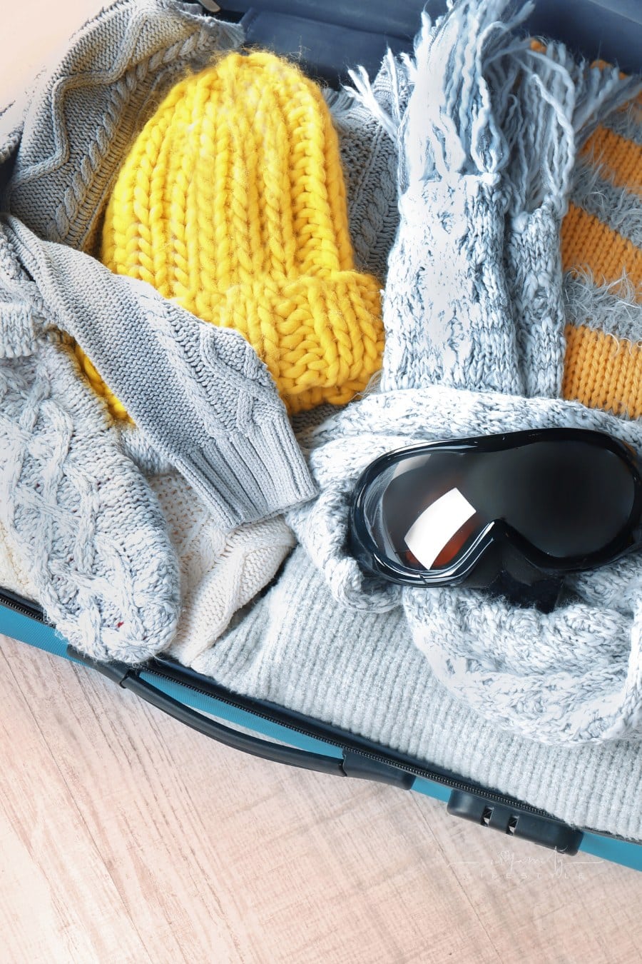 Open suitcase with warm clothes and ski goggles on wooden floor. Winter vacation concept