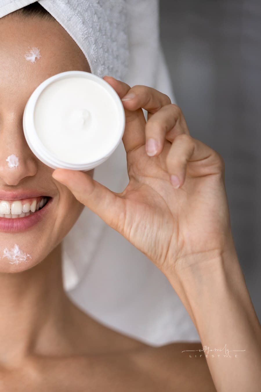 Smiling young woman using moisturizing face cream in bathroom