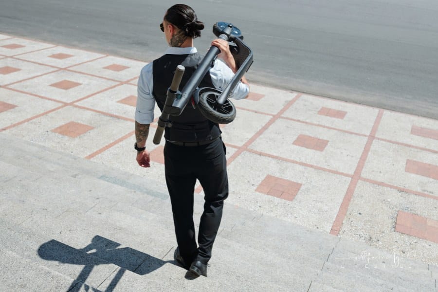 Man Carrying folded-up Electric Scooter down flight of stairs