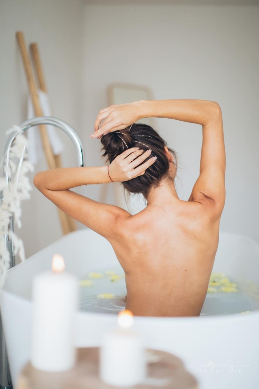 woman holding her hair bun with both hands while sitting in a tub filled with water and yellow flowers