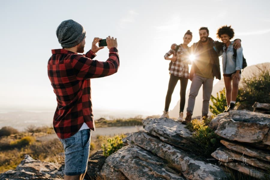 Group of friends standing outdoors taking picture by smartphone. Young people on mountain hike taking photographs.