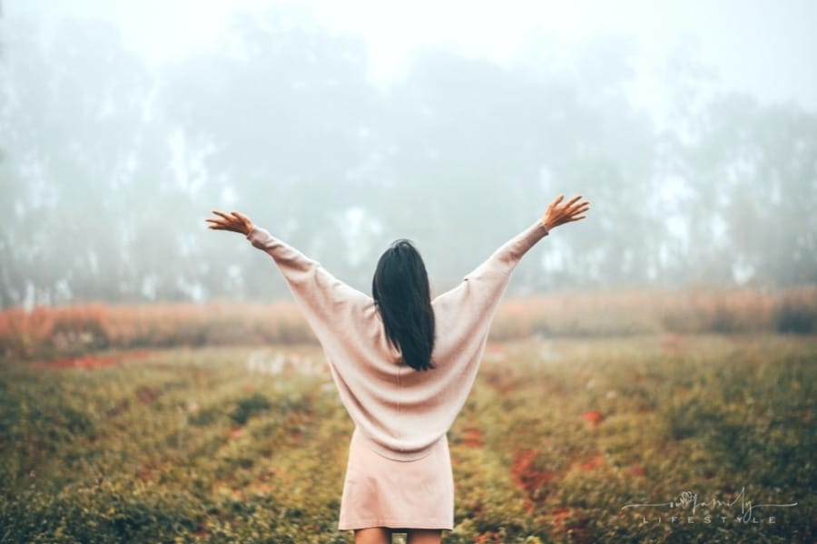 woman lifting hands into sky standing in field of flowers