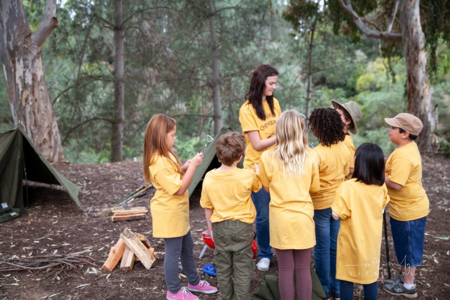 Summer camp counselor and kids in yellow t-shirts at campsite in woods
