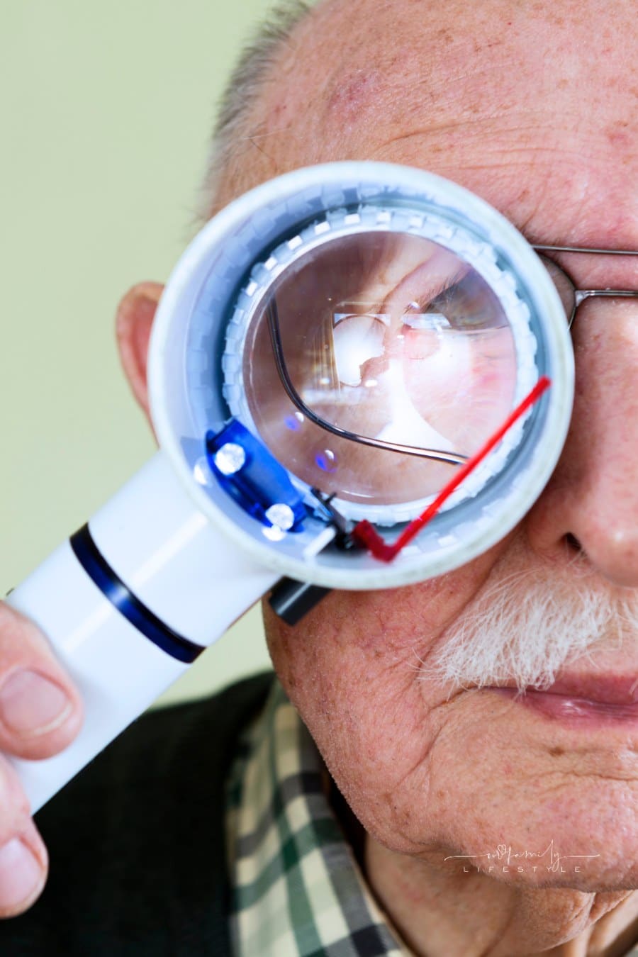 Senior man holding an illuminated magnifying glass he uses to help him read because he suffers from Wet Macular Degeneration.