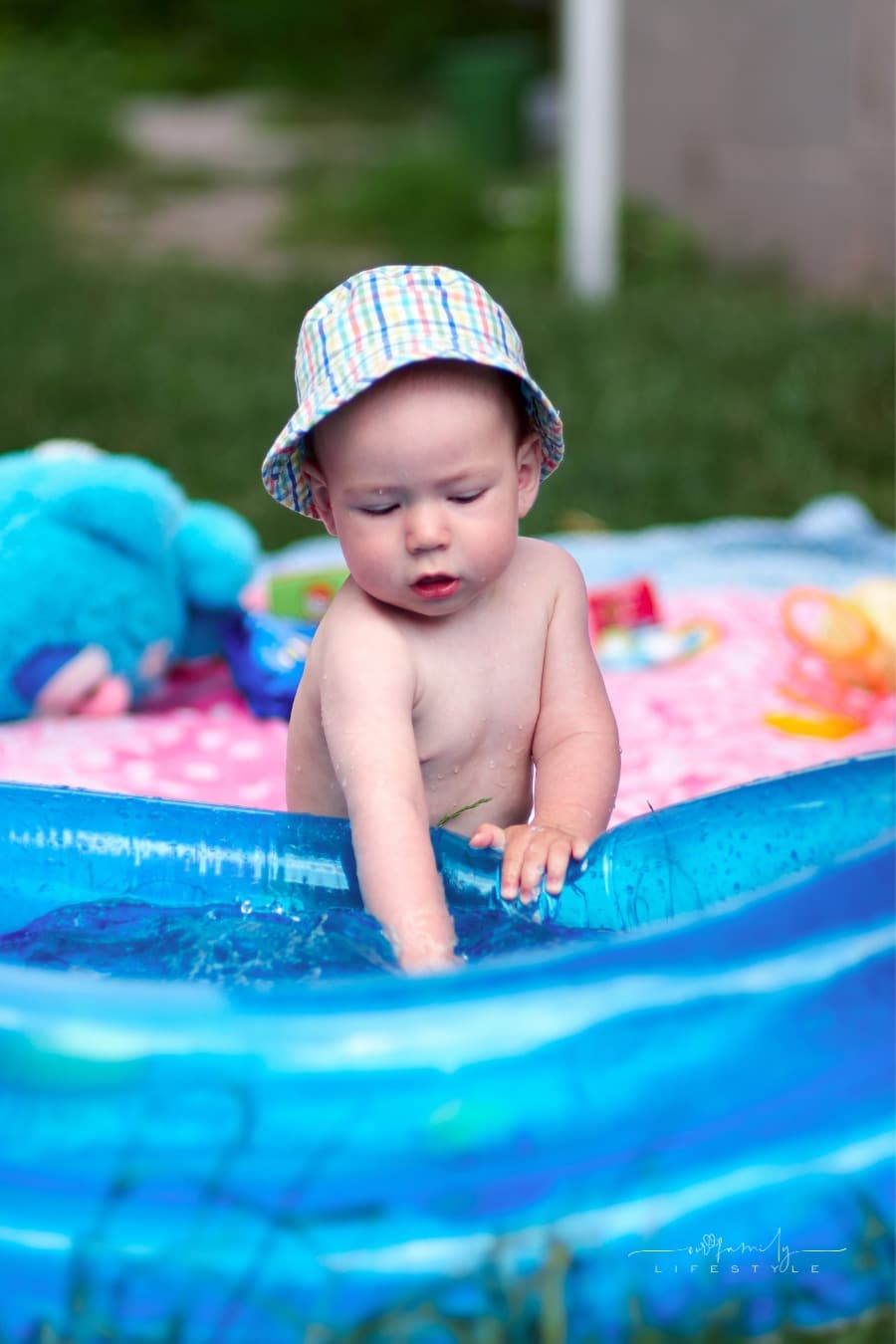 toddler with sun hat on playing with water inside an inflatable kiddie pool