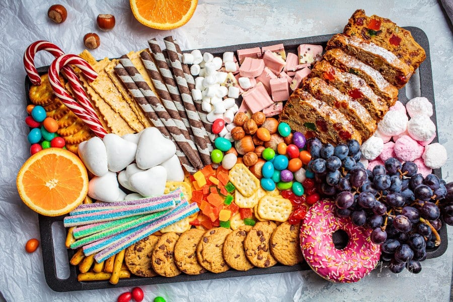 Christmas sweets platter. Christmas fruit cake, candy, chocolate, candy cane, cookies, fruit on black tray. Christmas food co