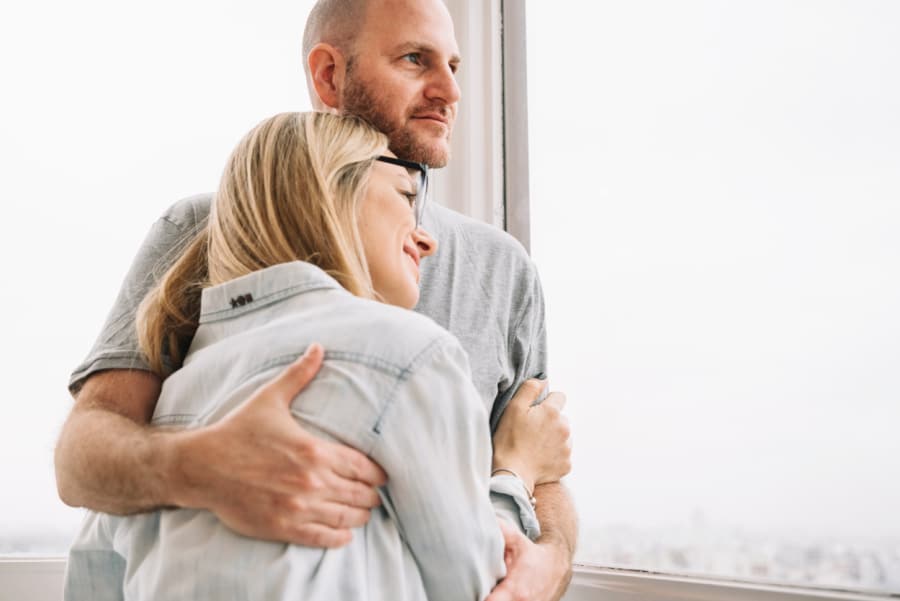 middle age married couple embracing while looking out window
