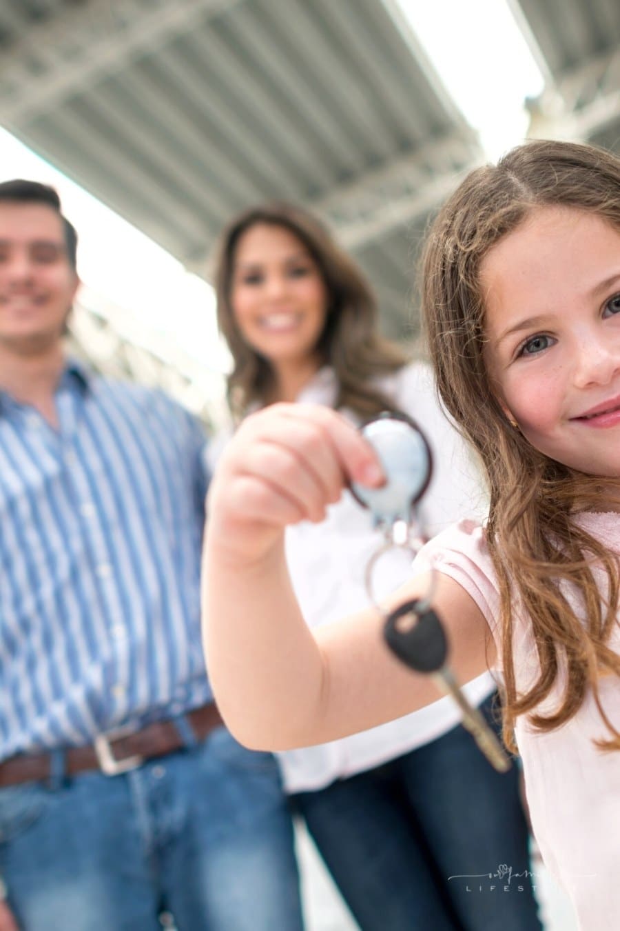 young girl holding out keys to new family car with parents in background
