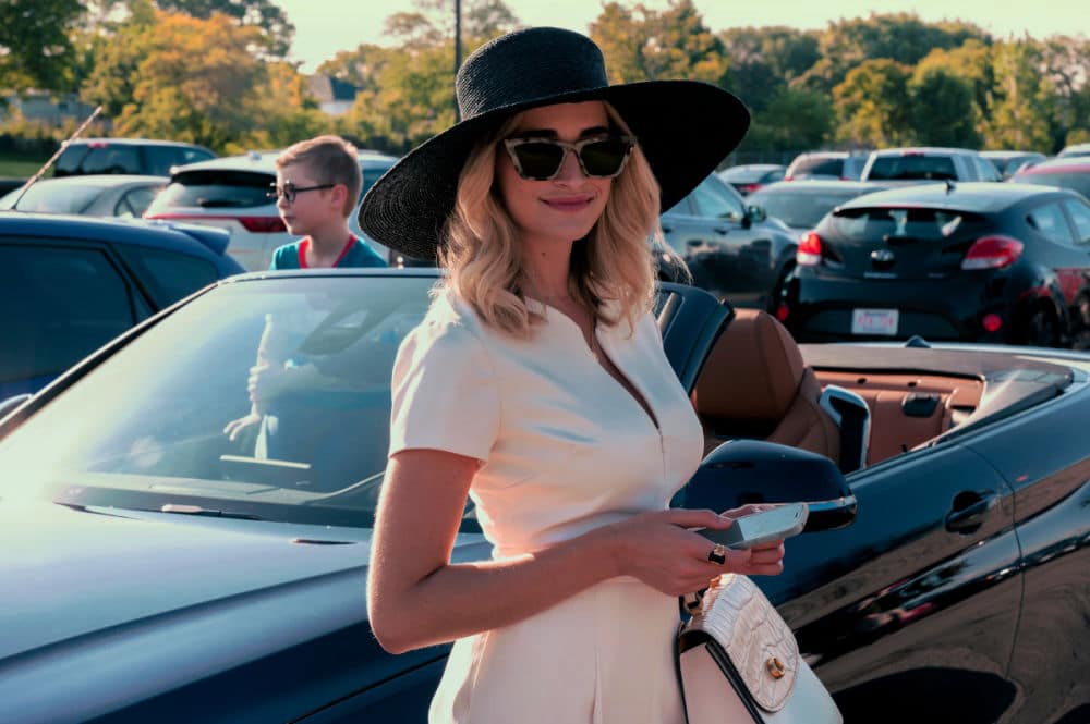 Scene from Netflix's series 'Ginny & Georgia,' featuring Georgia wearing a stylish hat and sunglasses, standing next to a convertible, reflecting her glamorous and mysterious personality.