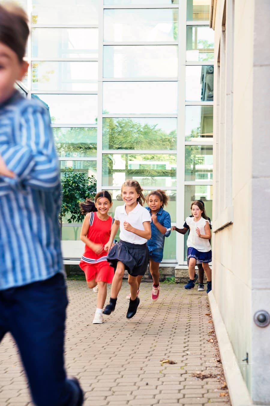 Elementary age kids running in school playground outdoors during recess.