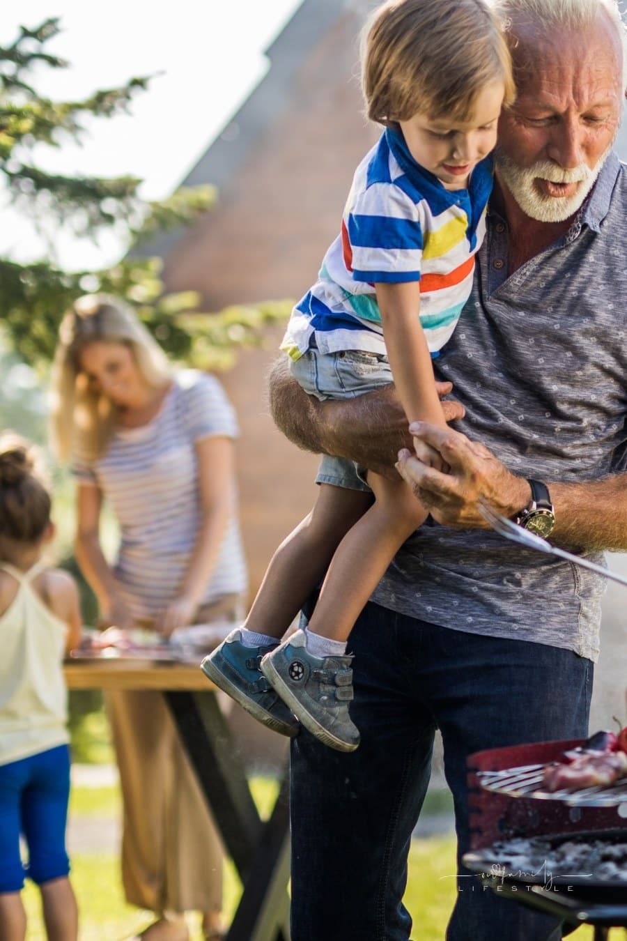 grandfather holding grandson while waiting for BBQ foods to cook over grill