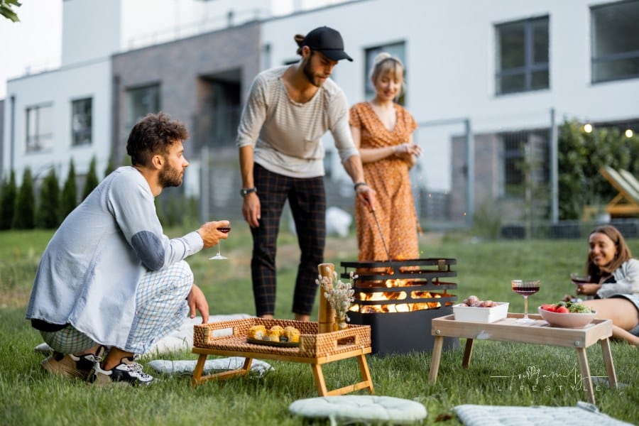Friends have a picnic, making fire at barbeque and talking on the green lawn at backyard of the country houses on the evening