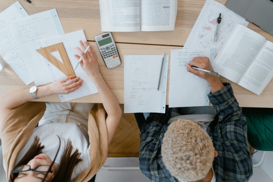 Overhead view of two students studying math with books, calculator, and geometry tools.