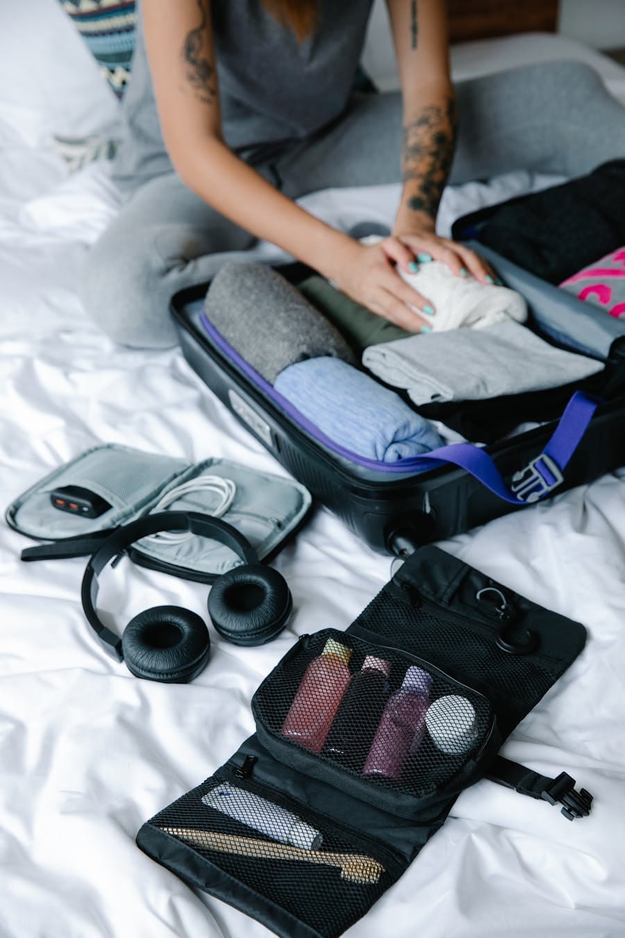 Person organizing suitcase with clothes and toiletries on bed, preparing for travel.