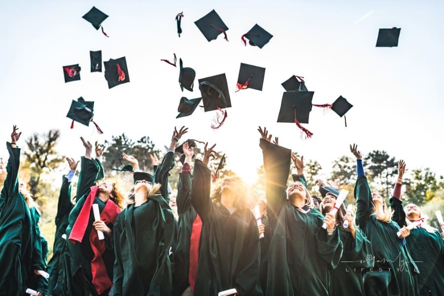 Large group of happy students celebrating their graduation day outdoors while throwing their caps up in the air.