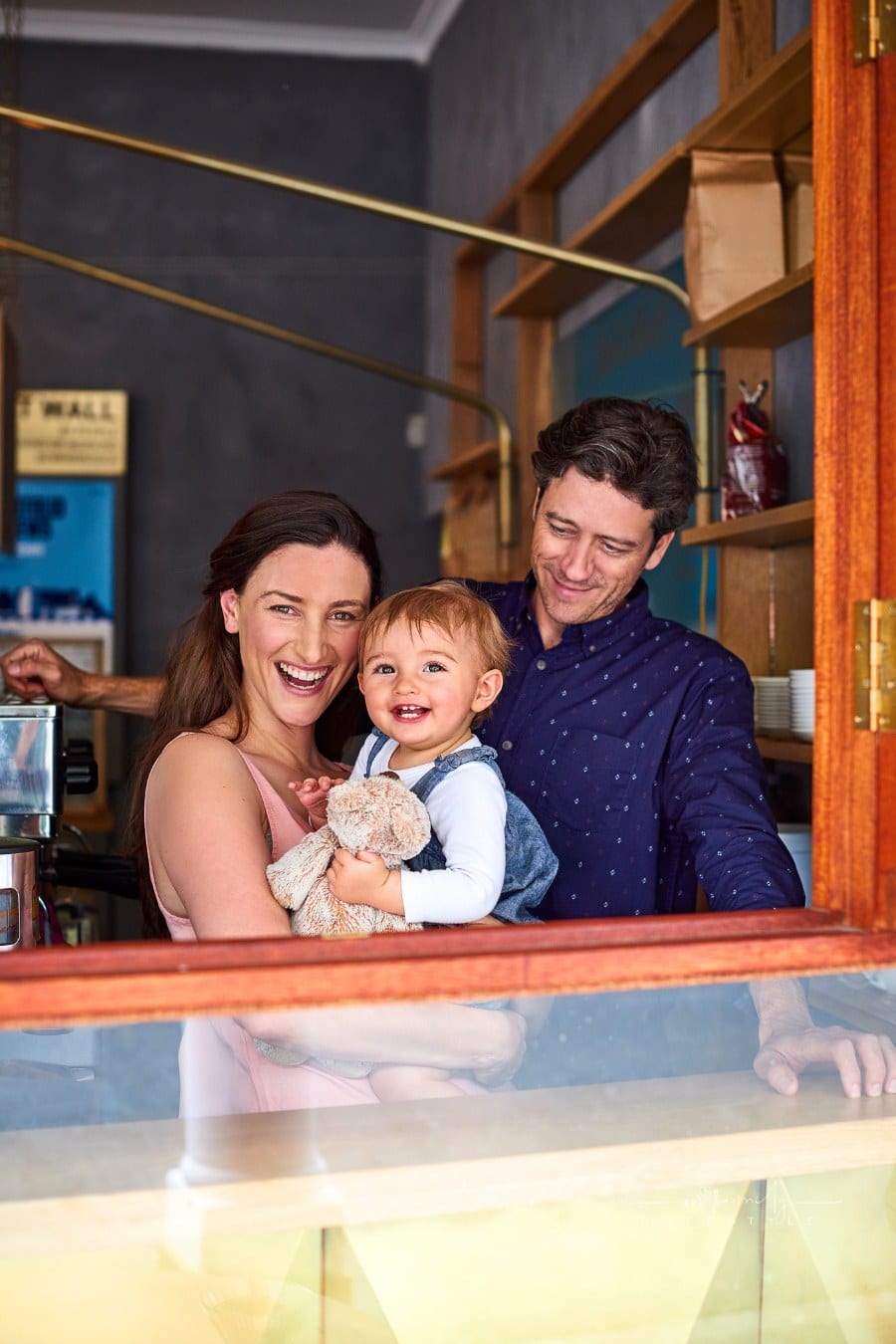 Portrait of smiling couple and their little girl looking through the window of their cafe