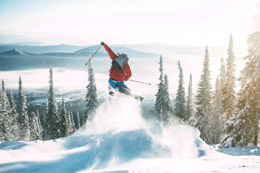 person jumping a snow bank while skiing